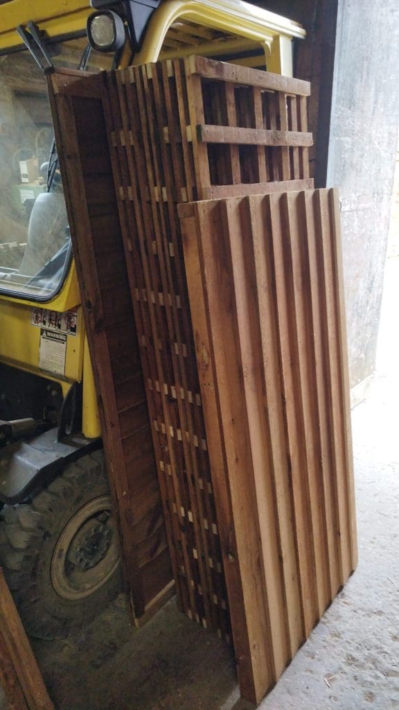 A stack of wooden pallets leaning against a yellow vehicle inside a dimly lit space. The pallets are arranged neatly and the vehicle is partially visible.