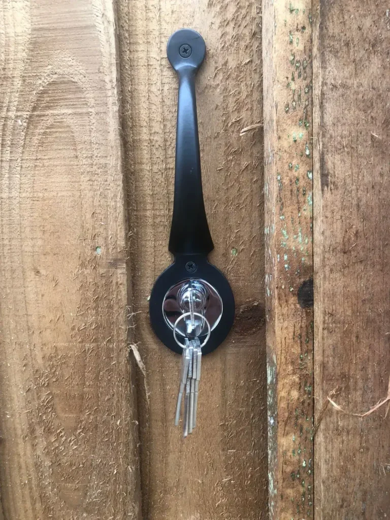 A black handle mounted on a wooden door holds a set of keys hanging from it. The wood shows signs of wear and weathering.